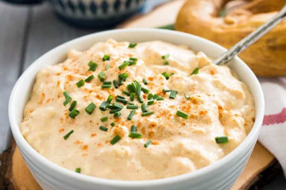 A white bowl filled with creamy cheese dip, topped with chopped chives and a sprinkle of paprika, with a spoon inside—an easy German food perfect for your Oktoberfest gatherings.