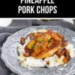 A plate of rice topped with pineapple pork chops, garnished with juicy pineapple chunks and sauce, served on a decorative gray plate.