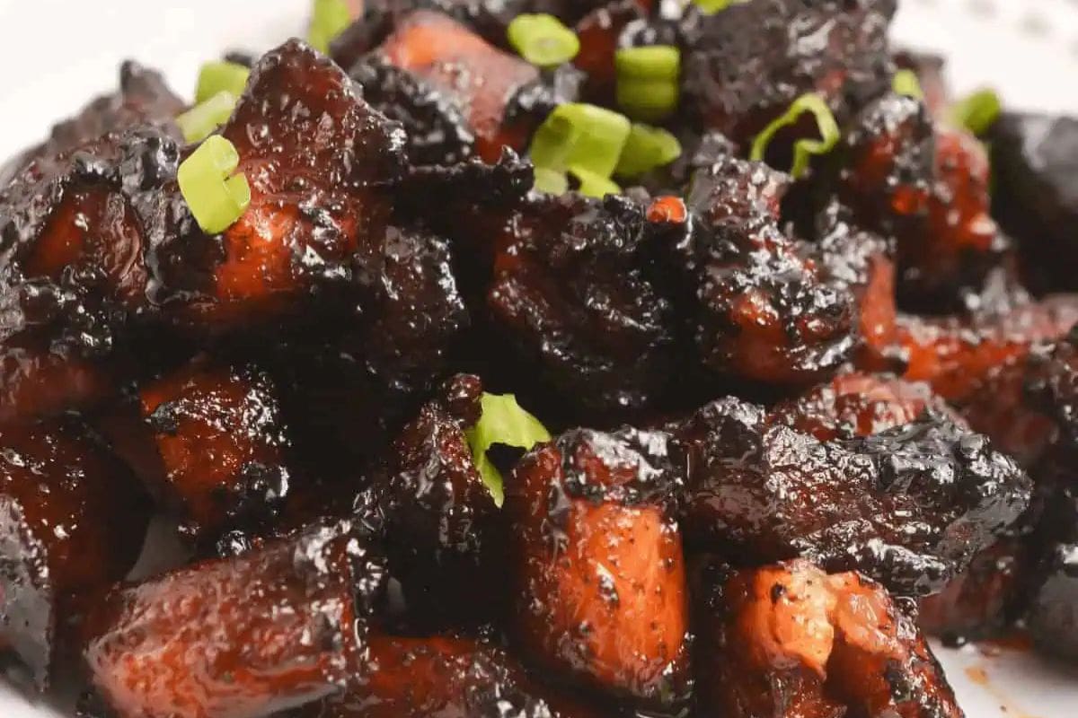 Close-up of caramelized pork belly pieces garnished with chopped green onions on a white plate—a mouthwatering addition to your Star Spangled BBQ and other All American recipes.