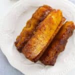 Three pieces of the fruit on a white decorative plate, placed on a light gray cloth next to a bowl of brown sugar.