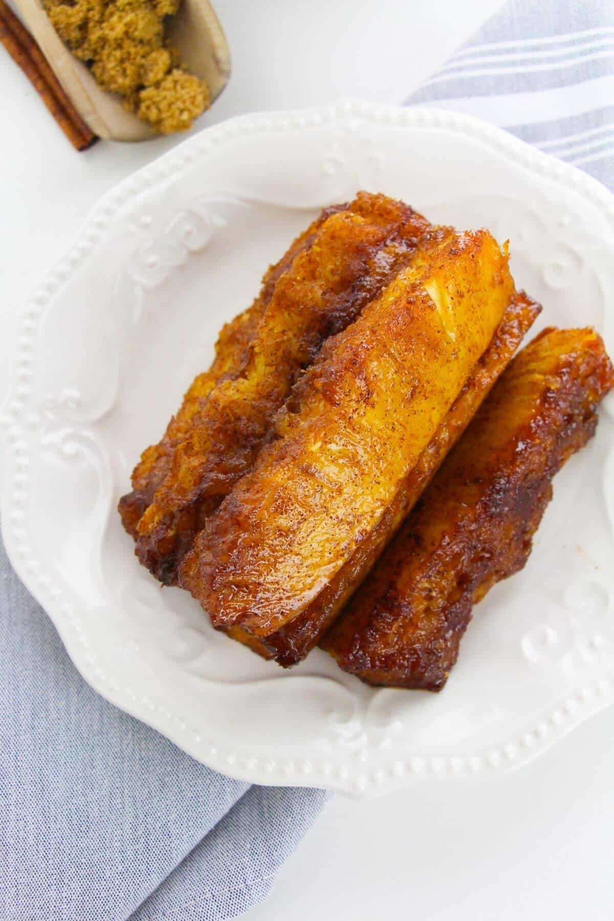 Three pieces of the fruit on a white decorative plate, placed on a light gray cloth next to a bowl of brown sugar.