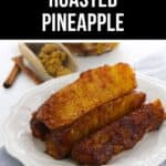 Three pieces of Roasted Pineapple are served on a white plate, with cinnamon sticks and brown sugar in the background for a touch of warmth and sweetness.
