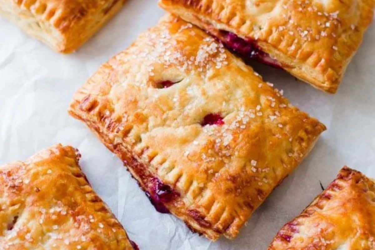 Golden brown hand pies with sugar crystals on top and vibrant berry filling peeking out—these fresh cherry recipes are perfect for showcasing juicy, fresh cherries on parchment paper.