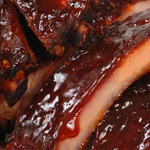 Close-up of glazed, barbecued pork ribs with a glossy sauce coating and visible char marks on the meat—a mouthwatering classic from our All American recipes collection.
