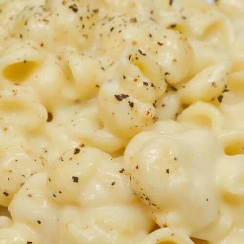 Close-up of creamy White Cheddar Mac and Cheese on a white plate, topped with a sprinkle of black pepper.