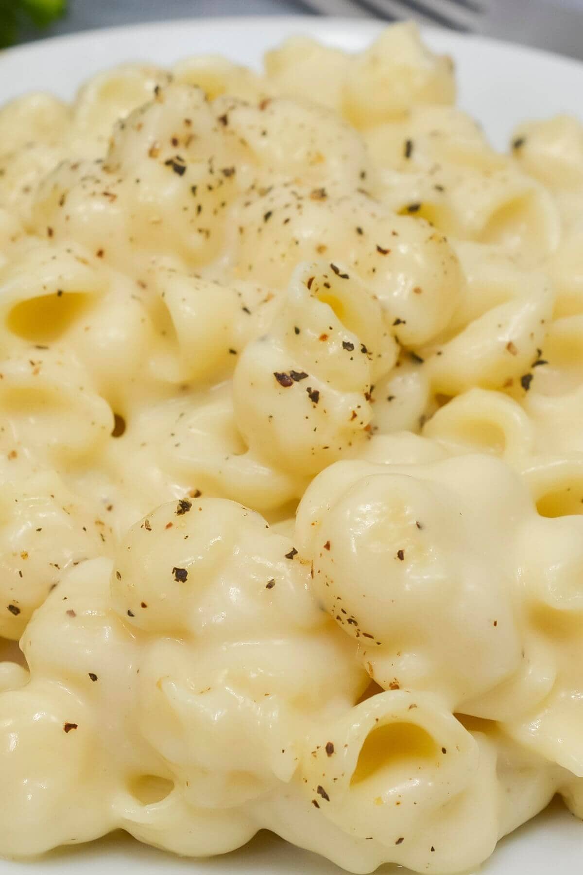 Close-up of creamy White Cheddar Mac and Cheese on a white plate, topped with a sprinkle of black pepper.