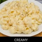 A plate of creamy White Cheddar Mac and Cheese is topped with ground black pepper, with parsley and a fork in the background.