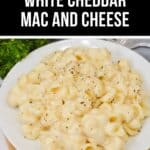 A plate of creamy White Cheddar Mac and Cheese, sprinkled with black pepper, sits on a white dish atop a wooden surface.