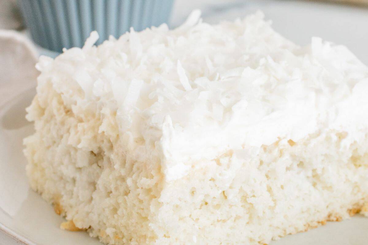 A close-up of a square slice of white cake topped with white frosting and shredded coconut on a plate—an irresistible coconut recipe perfect for any dessert lover.