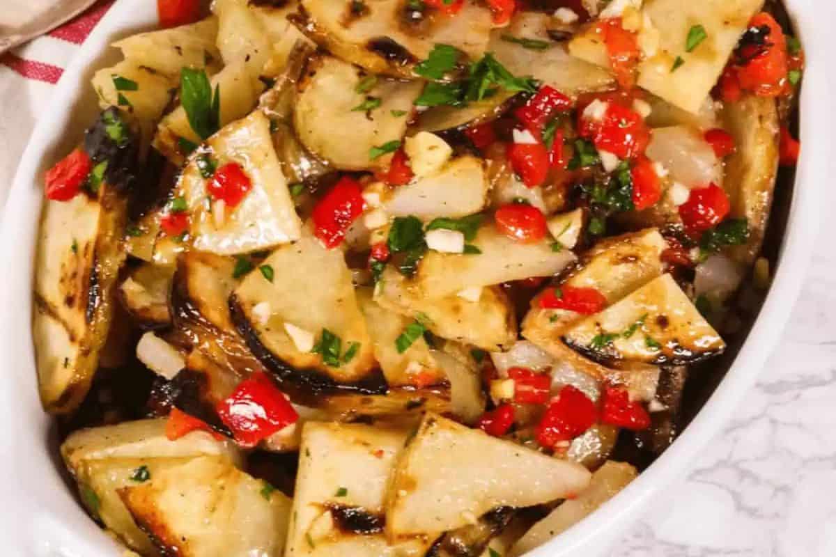 A dish of grilled potato slices mixed with chopped red peppers, onions, and parsley, served in a white oval bowl—one of our easy recipes inspired by Oktoberfest German favorites.