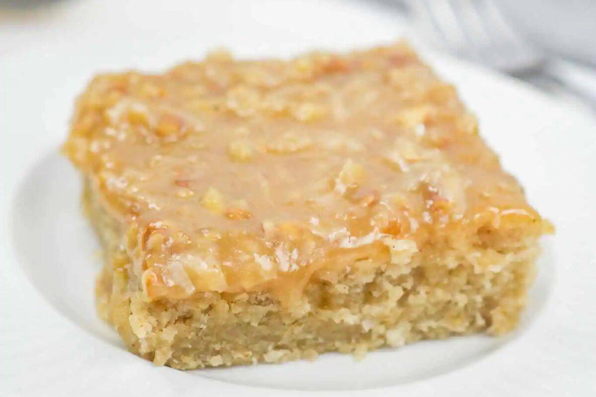 A square piece of cake with a light brown glaze sits on a white plate, showcasing one of the irresistible coconut dessert recipes that everyone will love.