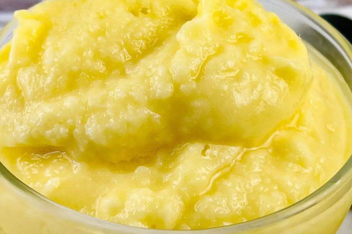 A close-up of a bowl filled with thick, yellow, creamy mashed potatoes or similar puree—perfect inspiration for easy dessert recipes or wow desserts for any summer gathering.