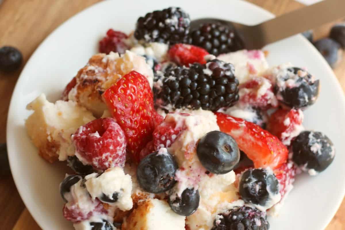 A close-up of a dessert plate with mixed berries, pieces of cake, and whipped cream, served with a spoon—perfect inspiration for wow desserts and easy dessert recipes.