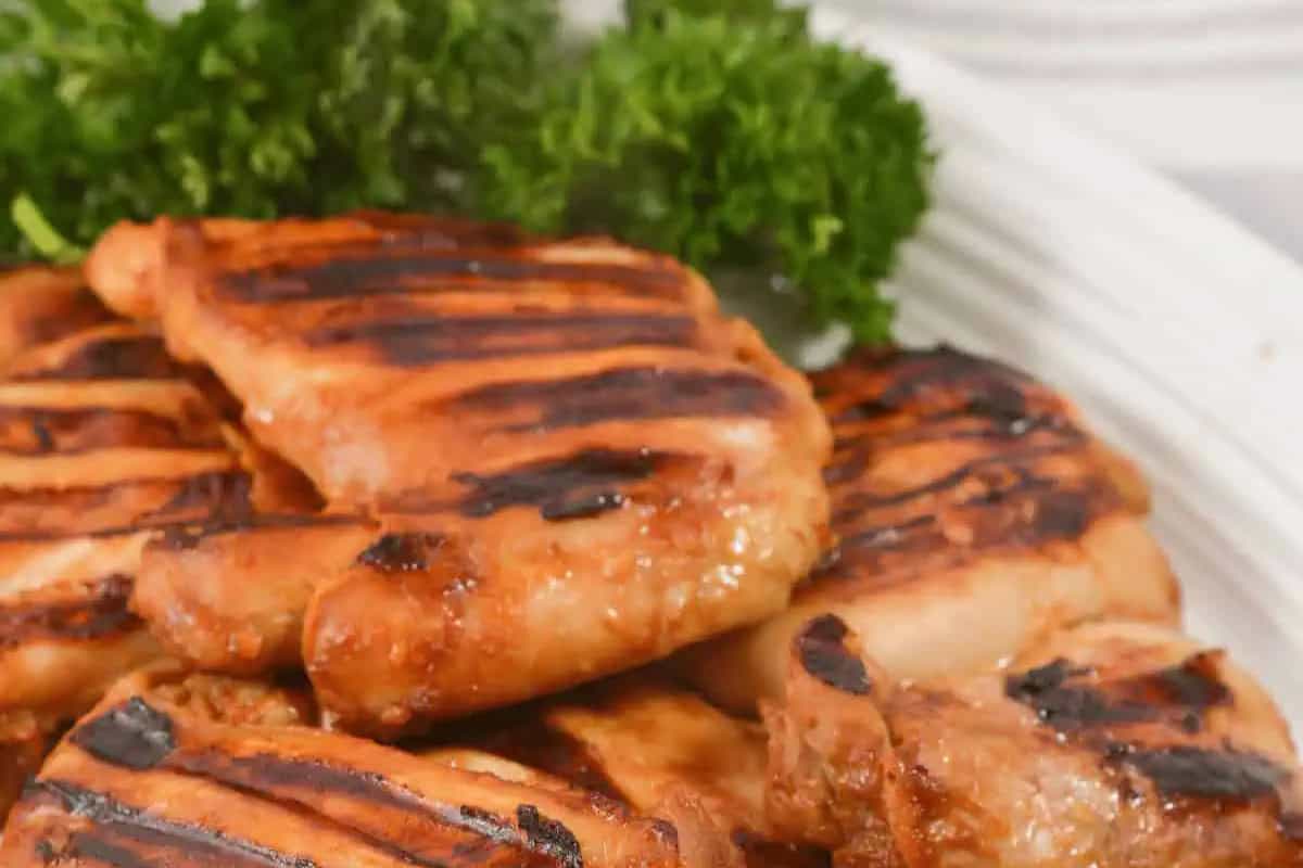 Grilled Chicken pieces with char marks are stacked on a plate, garnished with fresh parsley in the background—perfect inspiration for your next Grilled Chicken Recipes collection.