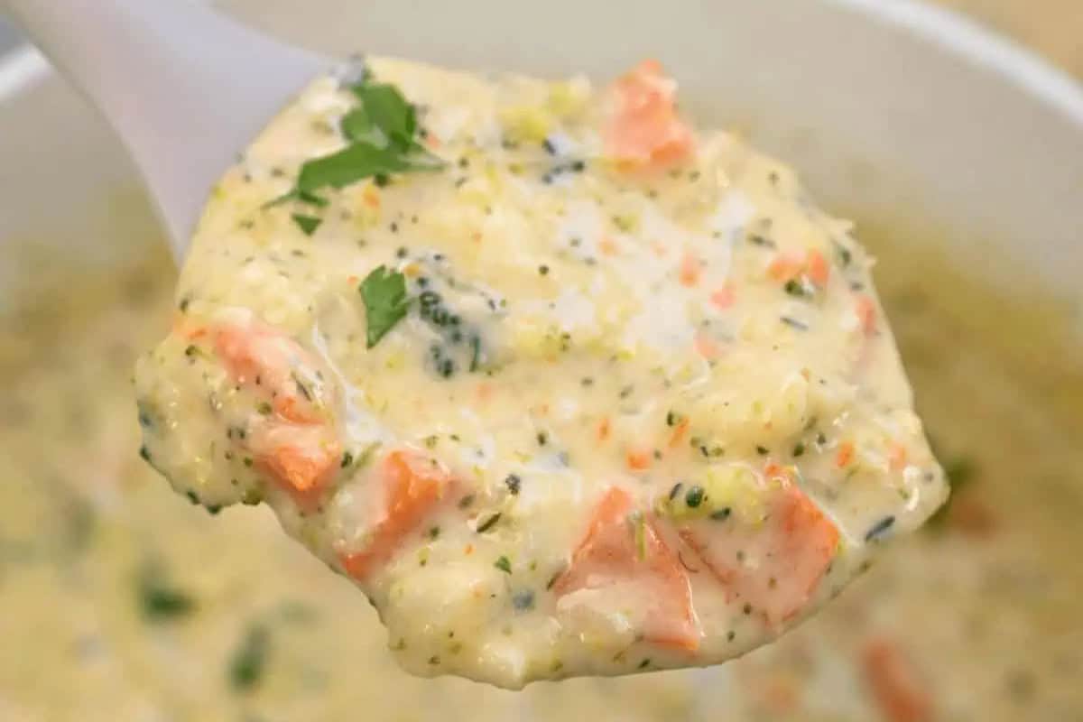 A close-up of a spoonful of creamy broccoli and carrot soup, garnished with chopped herbs—a delicious choice even for picky eaters.