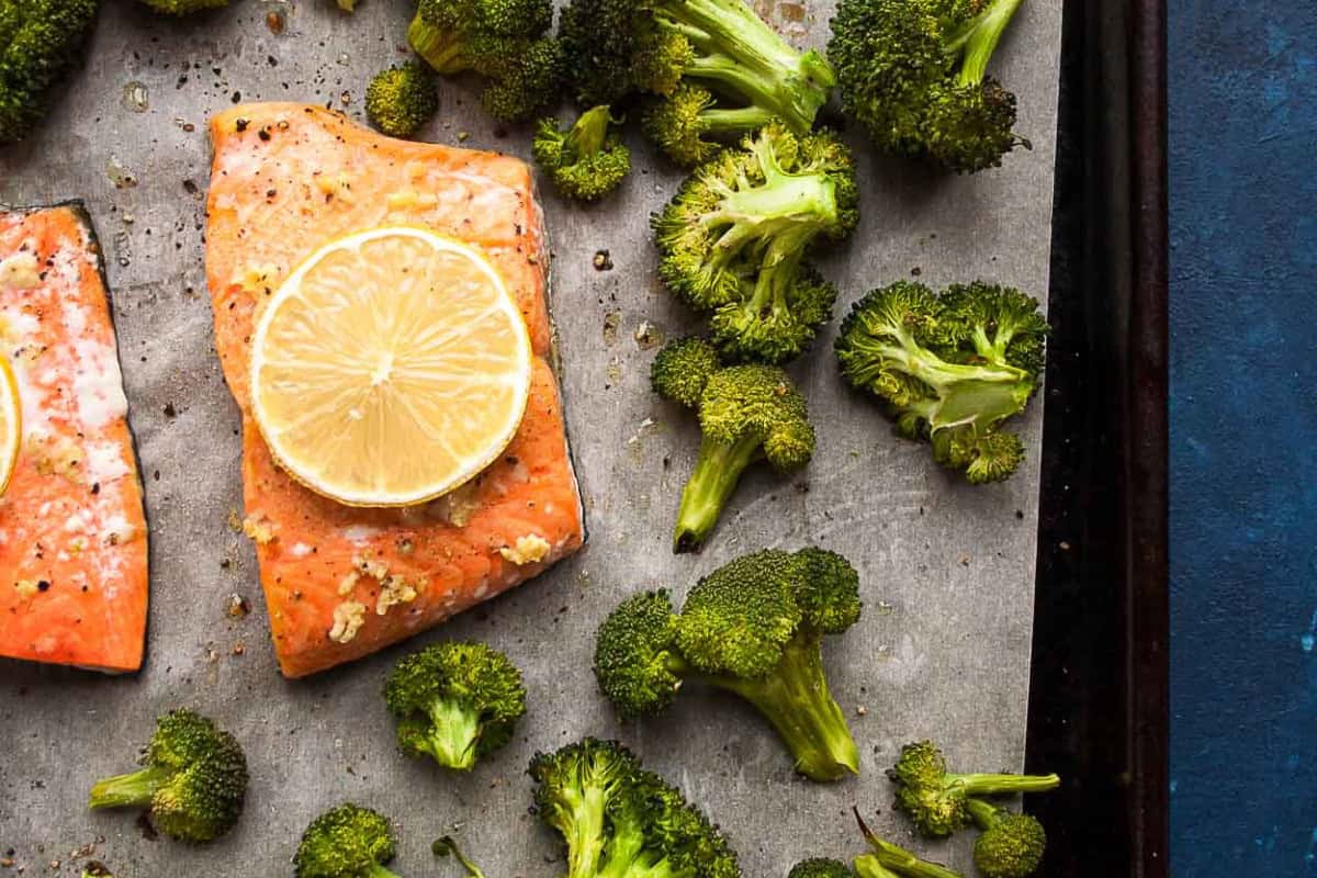 Baked salmon fillets topped with lemon slices and surrounded by roasted broccoli make a delicious meal—perfect for picky eaters looking to try new broccoli recipes.