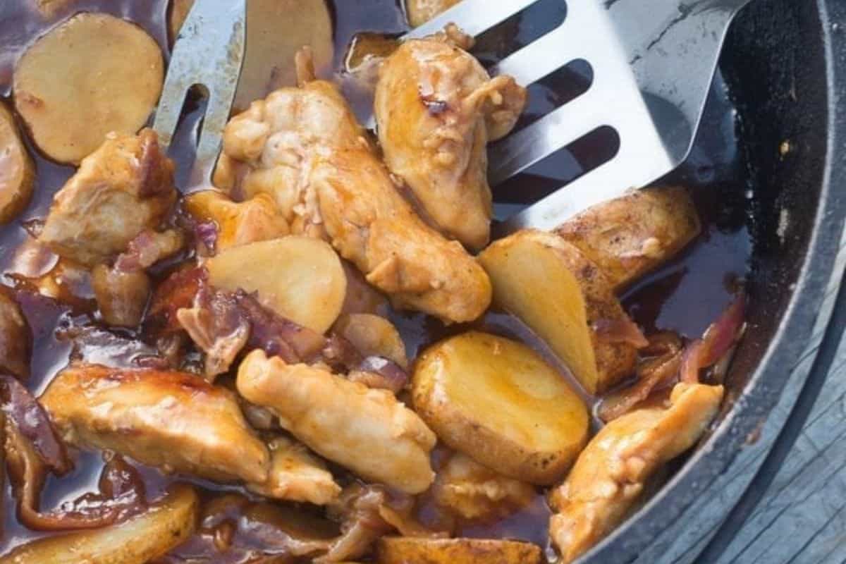 A close-up of BBQ chicken pieces and potato slices in a round dutch oven.