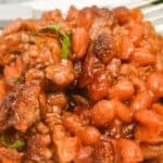 A white plate with baked beans with ground beef.
