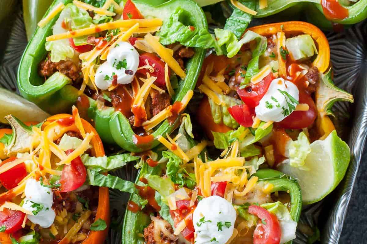 Close-up of some green and orange bell pepper halves, topped with ground beef, tomato, lettuce, cheese, and sour cream.
