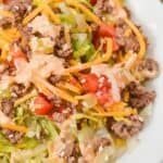 A plate of Big Mac Salad with ground beef, shredded cheddar cheese, chopped tomatoes, lettuce, sesame seeds, and creamy dressing.