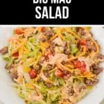 A bowl of Big Mac Salad with ground beef, shredded lettuce, cheddar cheese, diced tomatoes, pickles, and dressing is served on a white plate.