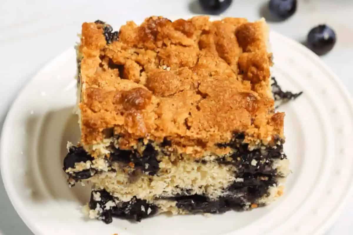 Close-up image of a slice of blueberry crumb cake, served on a white plate.