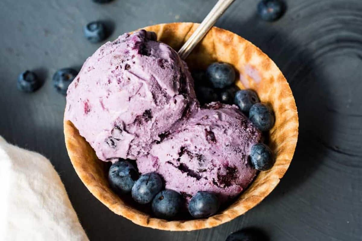 Close-up of two scoops of blueberry ice cream, garnished with blueberries and served in a waffle cone dish.