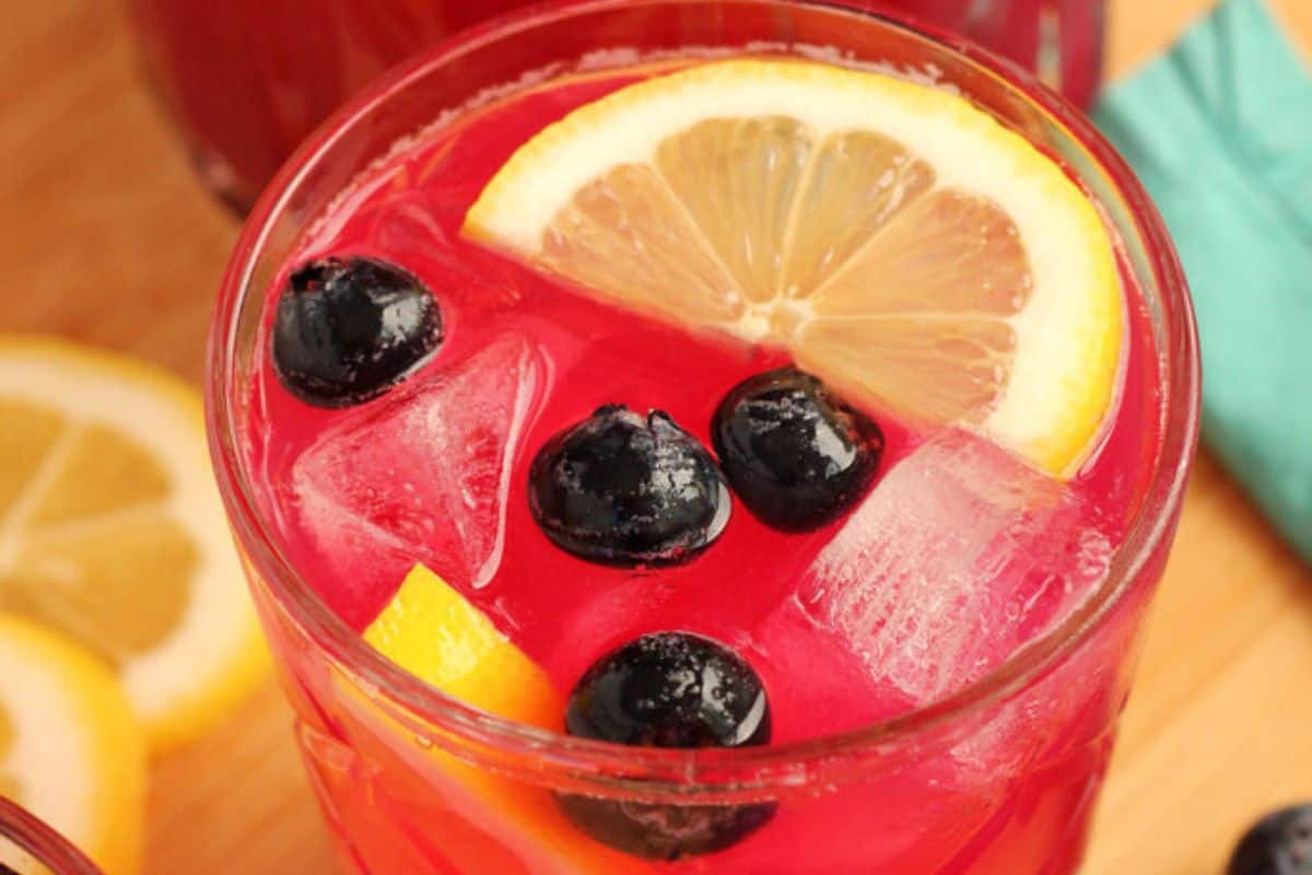 Close-up of. aglass of blueberry lemonade, garnished with blueberries and a lemon slice.