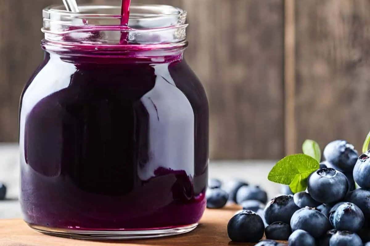 Close-up of a jar of blueberry syrup, whith a pile of blueberries next to it.