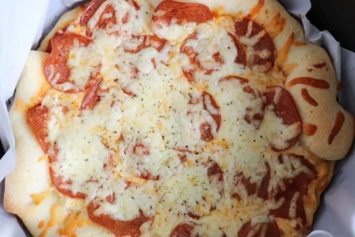A baked pepperoni pizza with melted cheese on top, set on parchment paper in a round pan—one of the best easy recipes for campfire cooking or Dutch oven recipes.