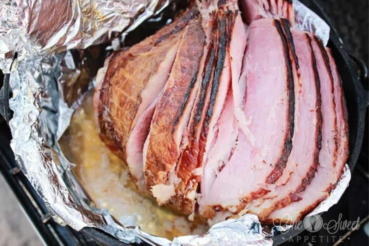 A sliced baked ham rests in a foil-lined pan, showing layers of pink meat and browned edges with visible juices at the bottom—perfect for easy recipes or comforting Dutch oven recipes.