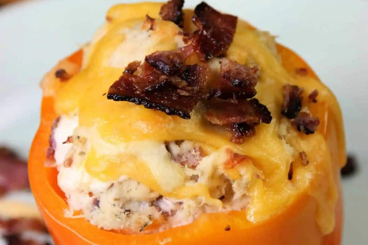 Close-up of an orange bell pepper, stuffed with chicken, cheese, and topped with bacon pieces.