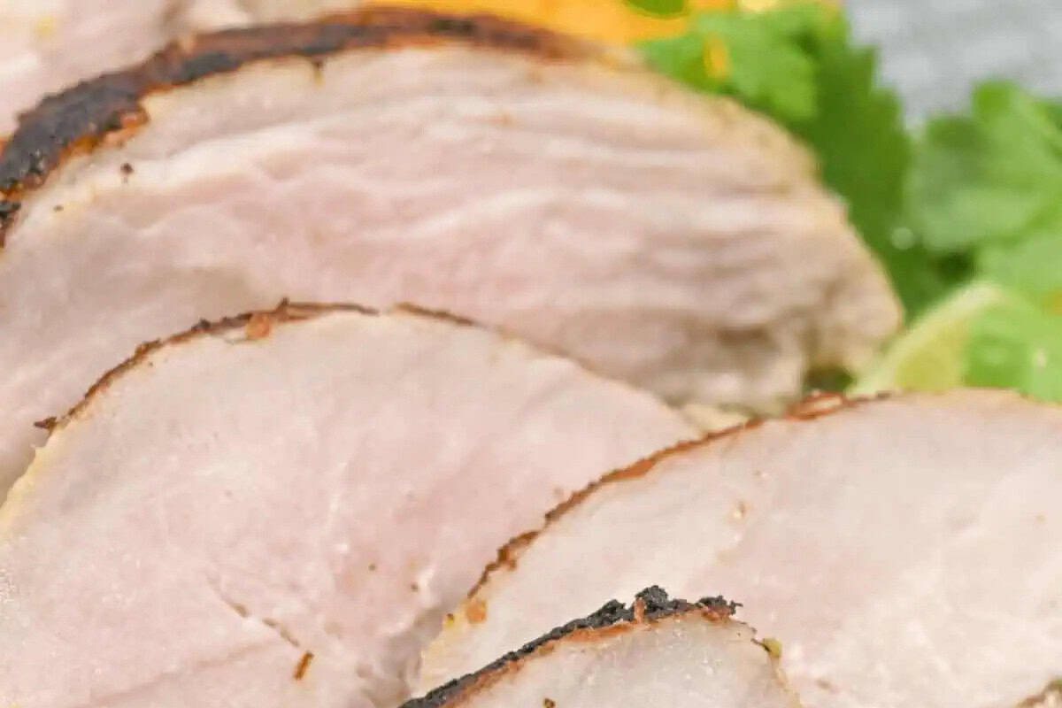Close-up of several slices of cooked pork with a browned edge, arranged overlapping on a plate with some green garnish visible in the background—a delicious choice for fans of Cuban cuisine and classic dinner recipes.