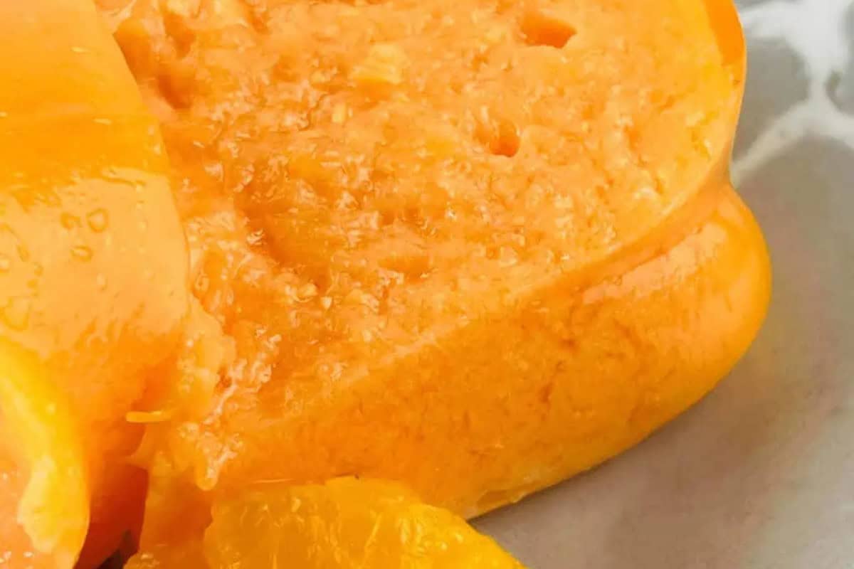 Close-up of a sliced orange Jello Salad dessert with a smooth, slightly textured surface, served with a piece of mandarin fruit—a nod to classic Vintage Jello Salad Recipes.