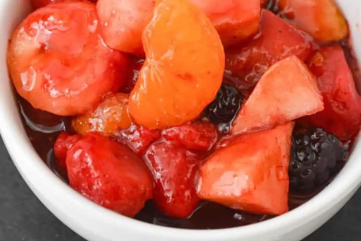 A close-up of a bowl filled with mixed fruit in syrup, including strawberries, blackberries, mandarin oranges, and pineapple chunks—perfect for recreating vintage Jello salad recipes.