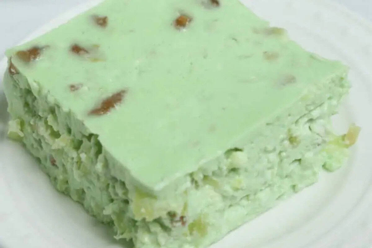 A square slice of light green gelatin dessert with chunks of fruit and nuts is served on a white plate, reminiscent of classic Vintage Jello Salad Recipes.