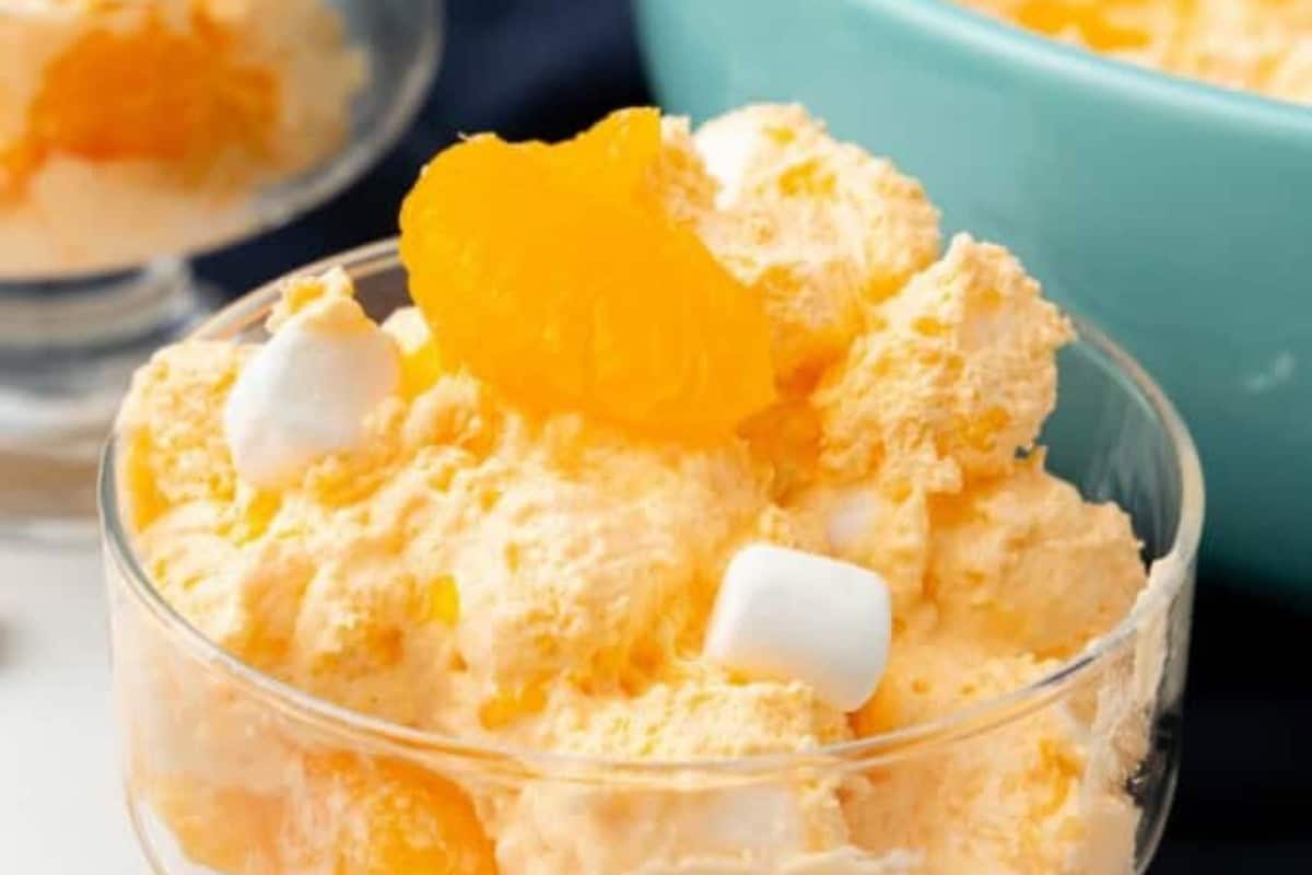 A glass bowl filled with orange fluff salad, featuring whipped cream, orange segments, and mini marshmallows—a sweet nod to classic Vintage Jello Salad Recipes.