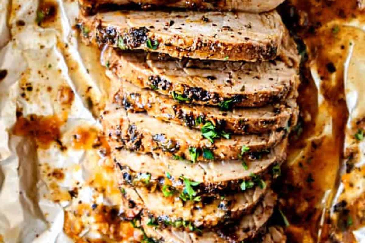 Slices of cooked pork tenderloin garnished with herbs are arranged on parchment paper with sauce—perfect for dinner and inspired by classic Cuban dishes.