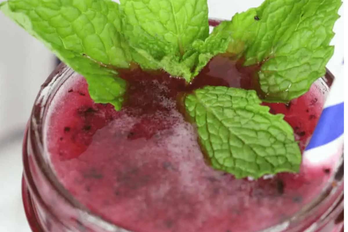 A close-up of a red moonshine beverage in a glass jar, garnished with fresh mint leaves and a blue-and-white striped straw—one of the must-try recipes for fans of flavored moonshine recipes.