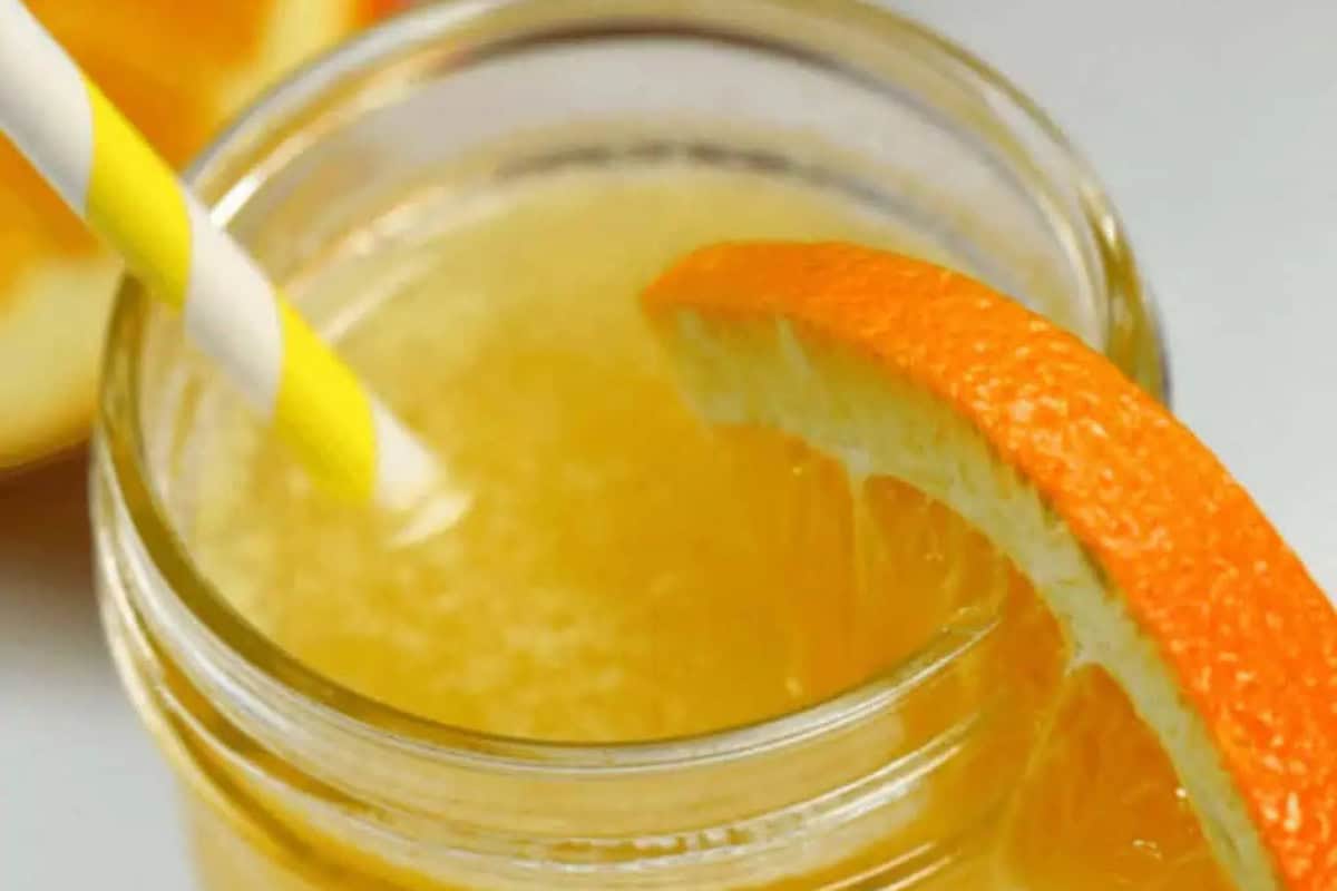 A glass of orange juice with a yellow-striped straw and an orange slice garnish on the rim—this must-try drink is perfect for experimenting with your favorite flavored moonshine recipes.