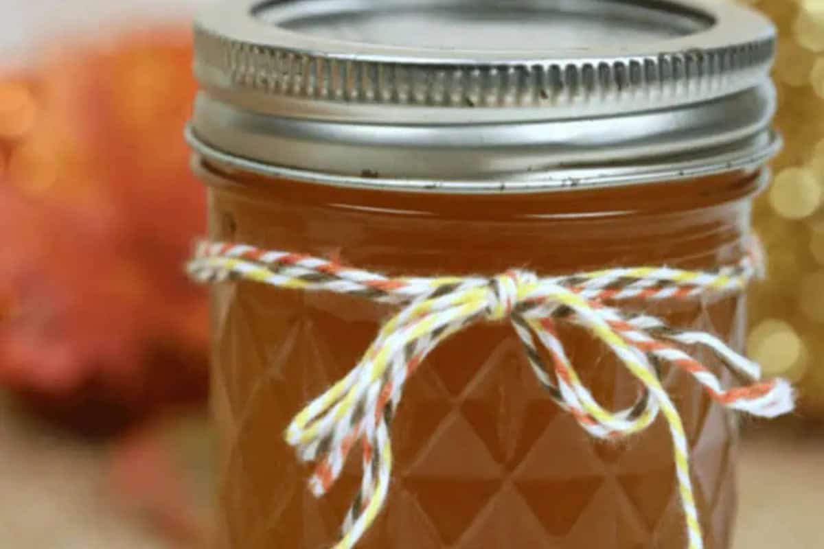 A glass jar filled with orange liquid, sealed with a metal lid and decorated with a yellow, orange, and white string bow—perfect for showcasing your favorite flavored moonshine recipes.