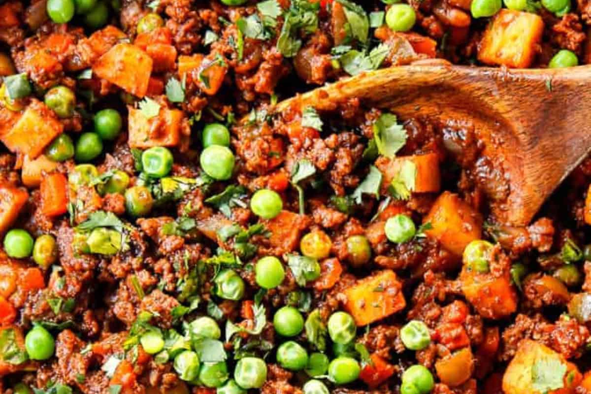 Ground meat cooked with diced potatoes, green peas, chopped herbs, and spices, being stirred with a wooden spoon—a classic example of Cuban cuisine perfect for those seeking authentic dinner recipes.