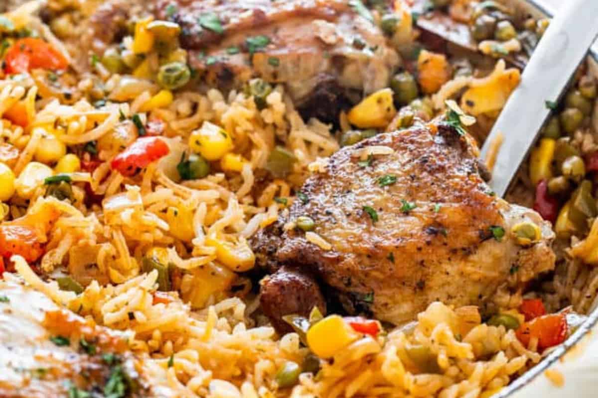 A close-up of seasoned chicken thighs served over rice mixed with corn, peas, carrots, and diced red bell peppers—a vibrant dinner inspired by classic Cuban dishes.
