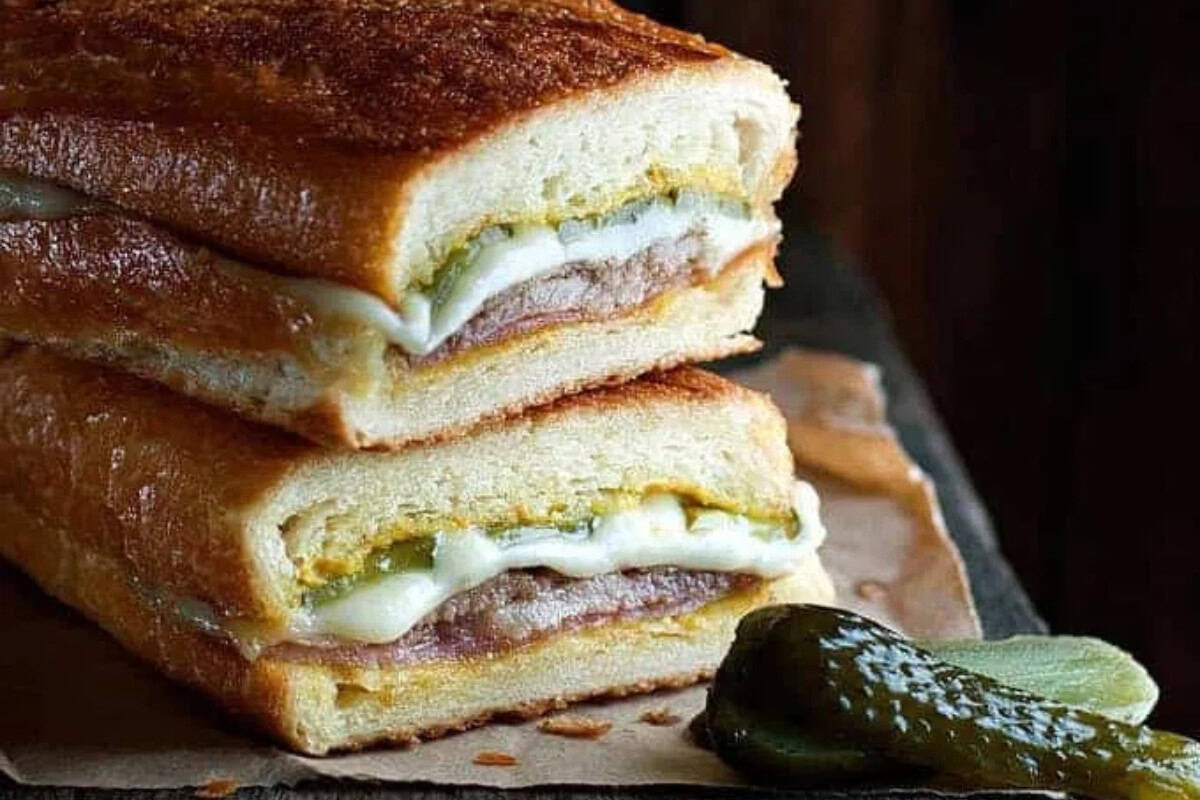 A close-up of a Cuban sandwich cut in half, showing layers of bread, cheese, pickles, and meat—a classic among Cuban dishes—served with a sliced pickle on the side, perfect for a savory dinner.