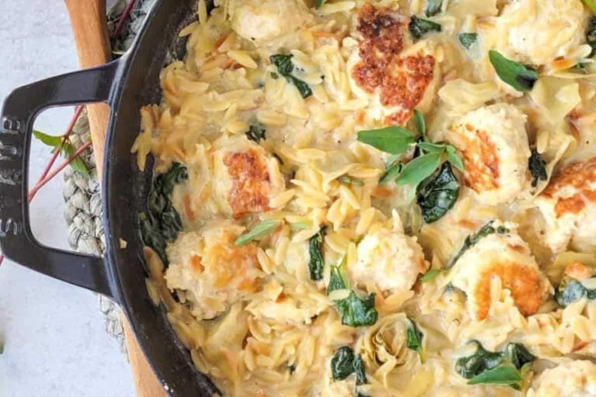 A skillet filled with creamy orzo pasta, spinach, and browned dumplings garnished with fresh herbs—an easy spinach recipe even picky eaters will love.