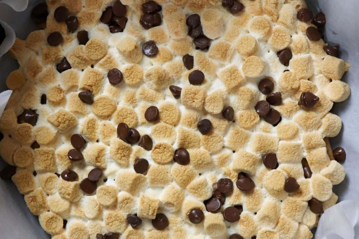A close-up of toasted mini marshmallows and chocolate chips on a baked dessert in a parchment-lined pan, perfect for fans of easy recipes or those who love campfire cooking treats.