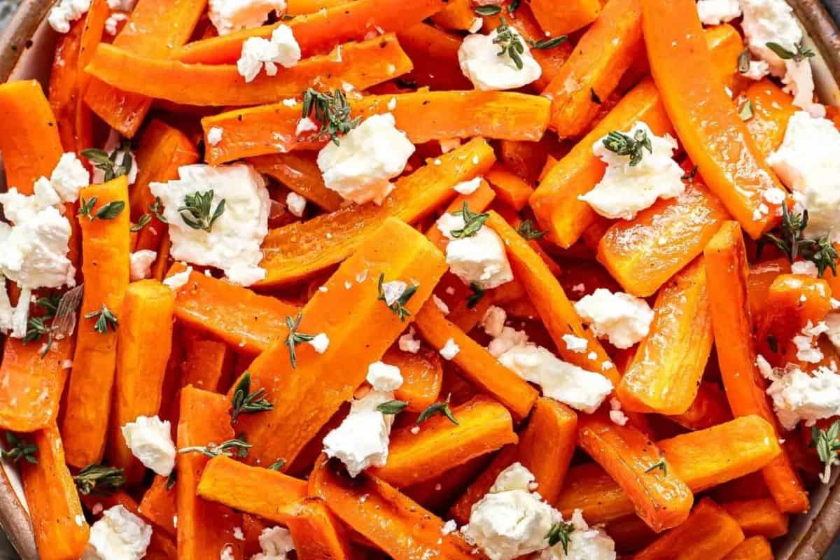 A pile of honey-roasted carrot sticks topped with crumbled white goat cheese and fresh thyme sprigs.