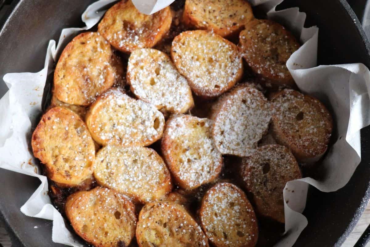 Slices of baked bread arranged in a parchment-lined dish, lightly dusted with powdered sugar—a cozy treat perfect for campfire cooking or adding to your collection of easy recipes.