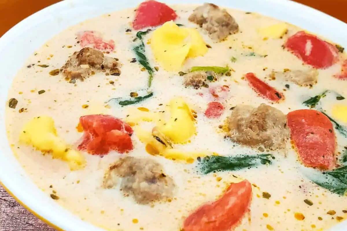 A bowl of creamy soup containing meatballs, spinach, tomato pieces, and cheese tortellini, garnished with herbs—one of the best easy spinach recipes for picky eaters.