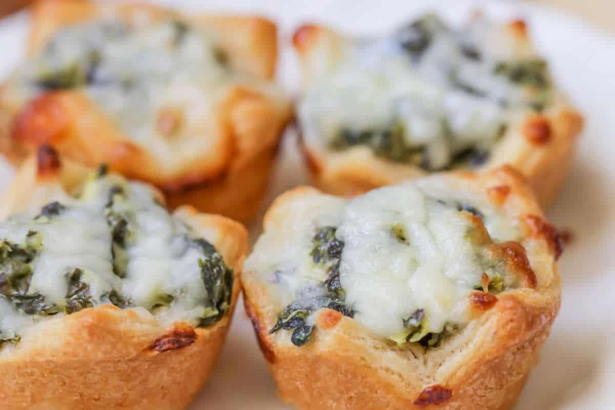 Four baked spinach and cheese puff pastry cups on a white plate—these easy spinach recipes are perfect for picky eaters.